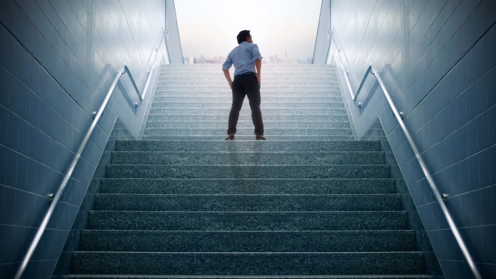 איש עסקים טיפס על גבי המדרגות הולך לעיר, קונספט שאיפות ועסקים הצלחה.